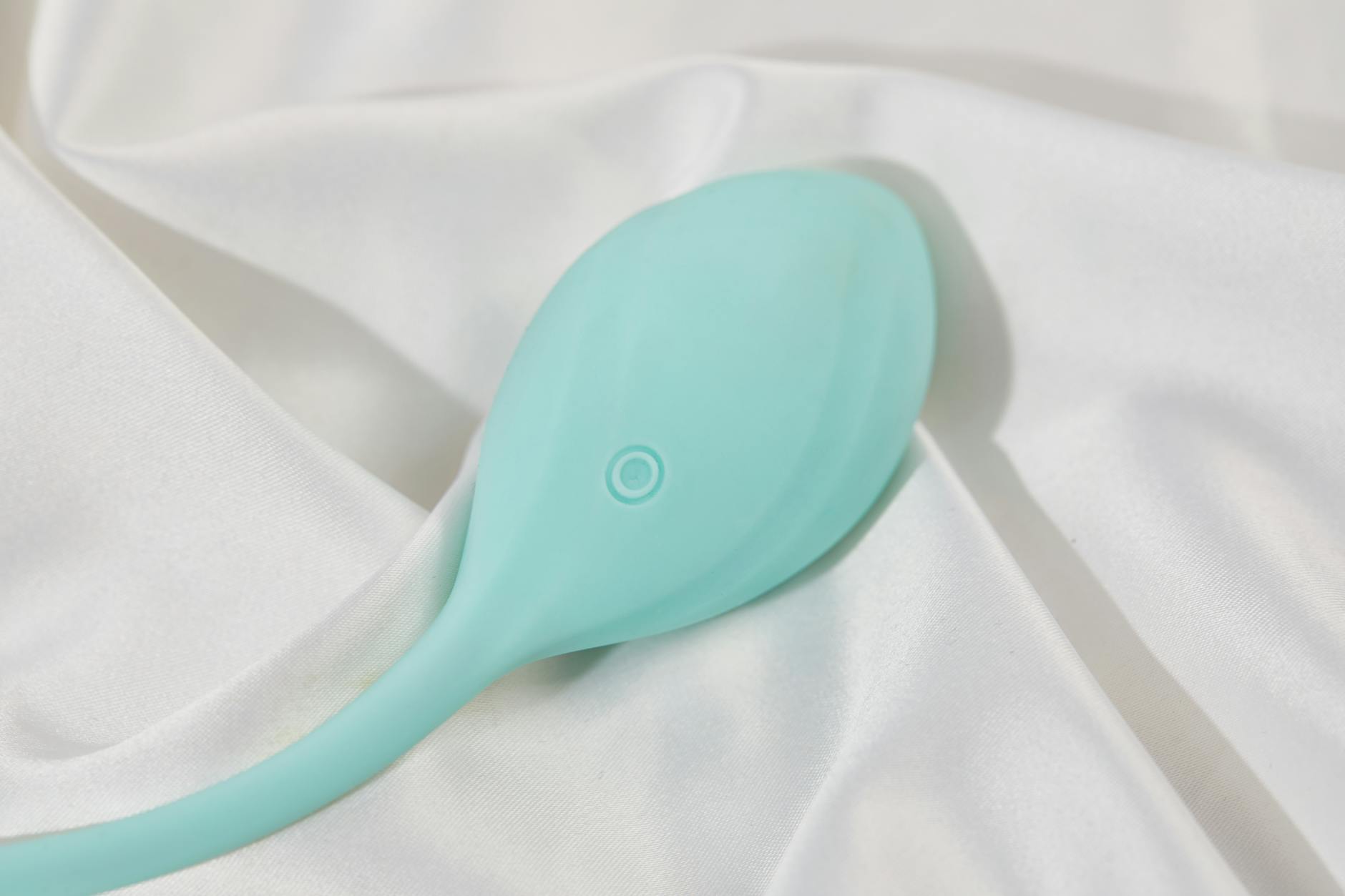 A teal suction vibrator on soft white silk fabric, symbolizing gentle intimacy during hormonal transitions