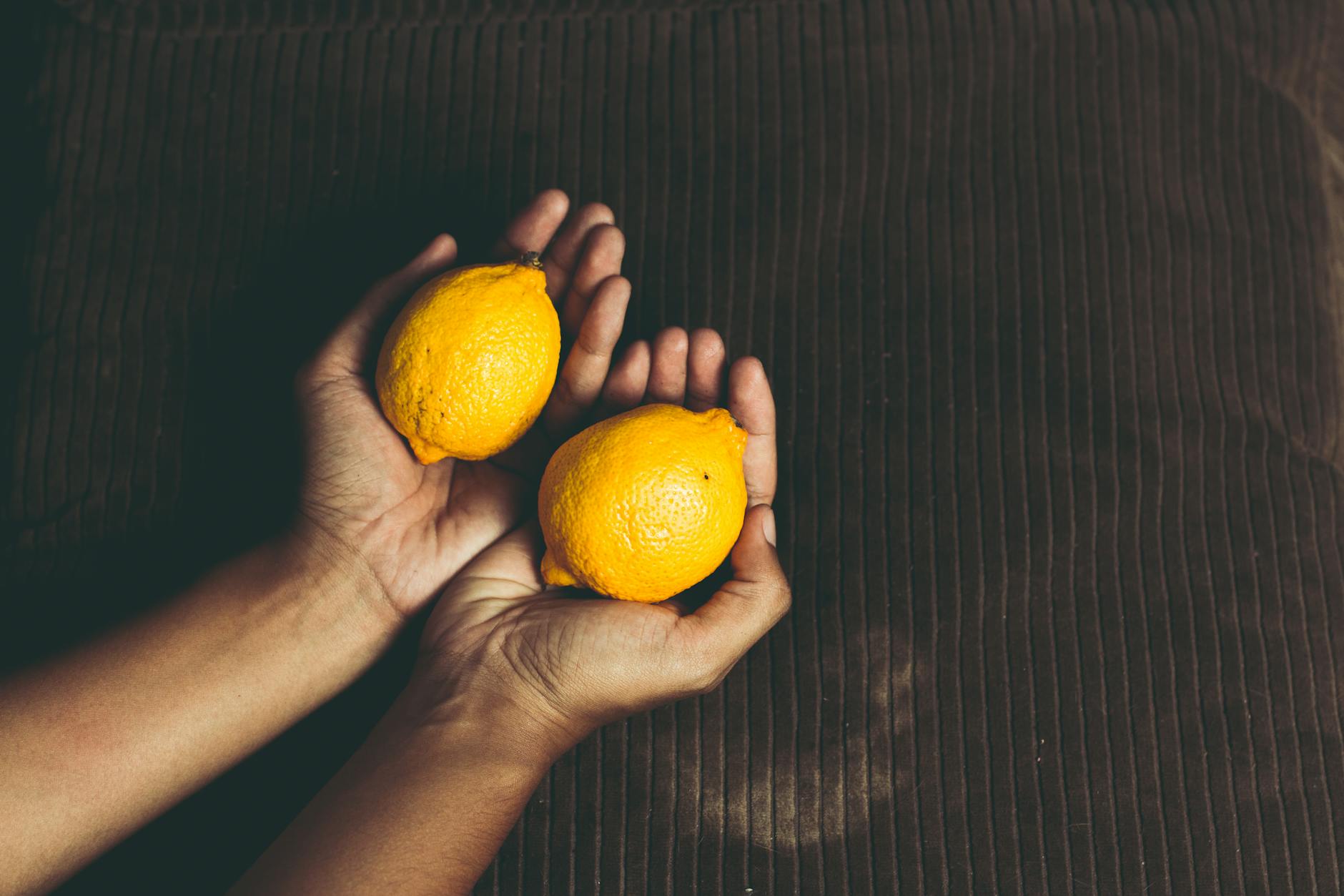 Hand holding a fresh lemon on soft pink background, symbolizing gentle postpartum healing