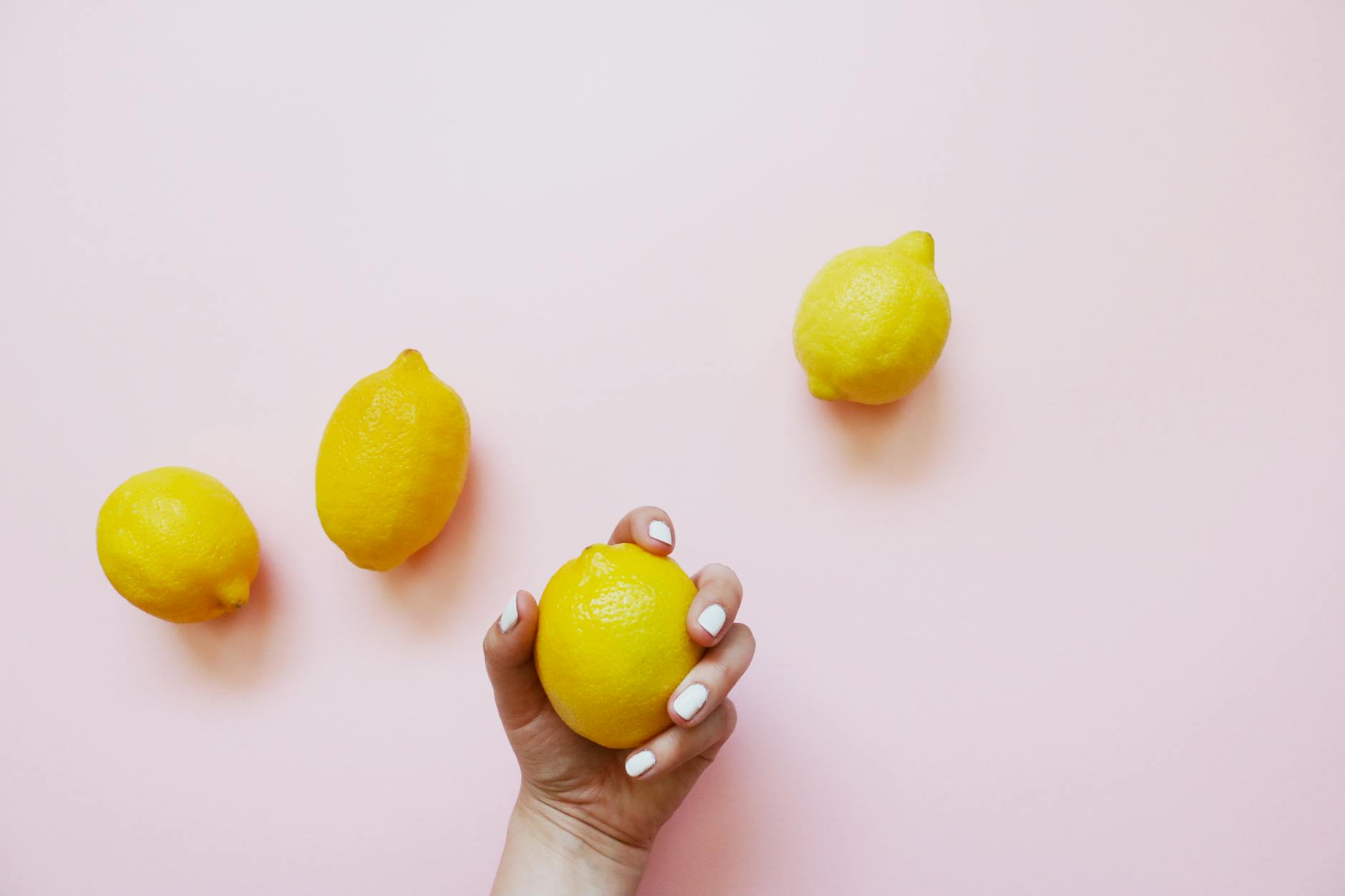 A hand holding a fresh lemon on a soft pink background