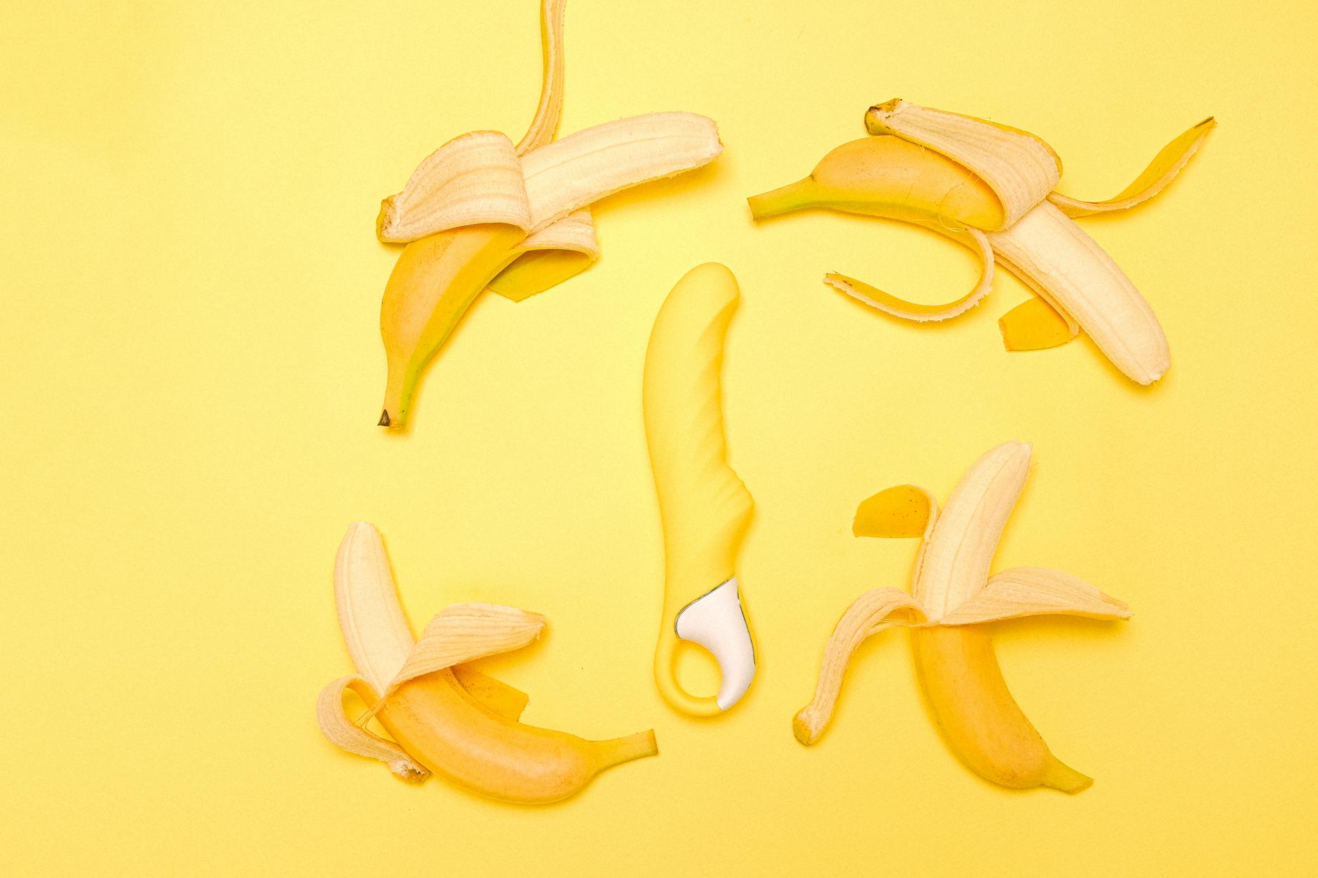 Yellow lemon vibrator surrounded by fresh lemons and fruit on a bright yellow surface