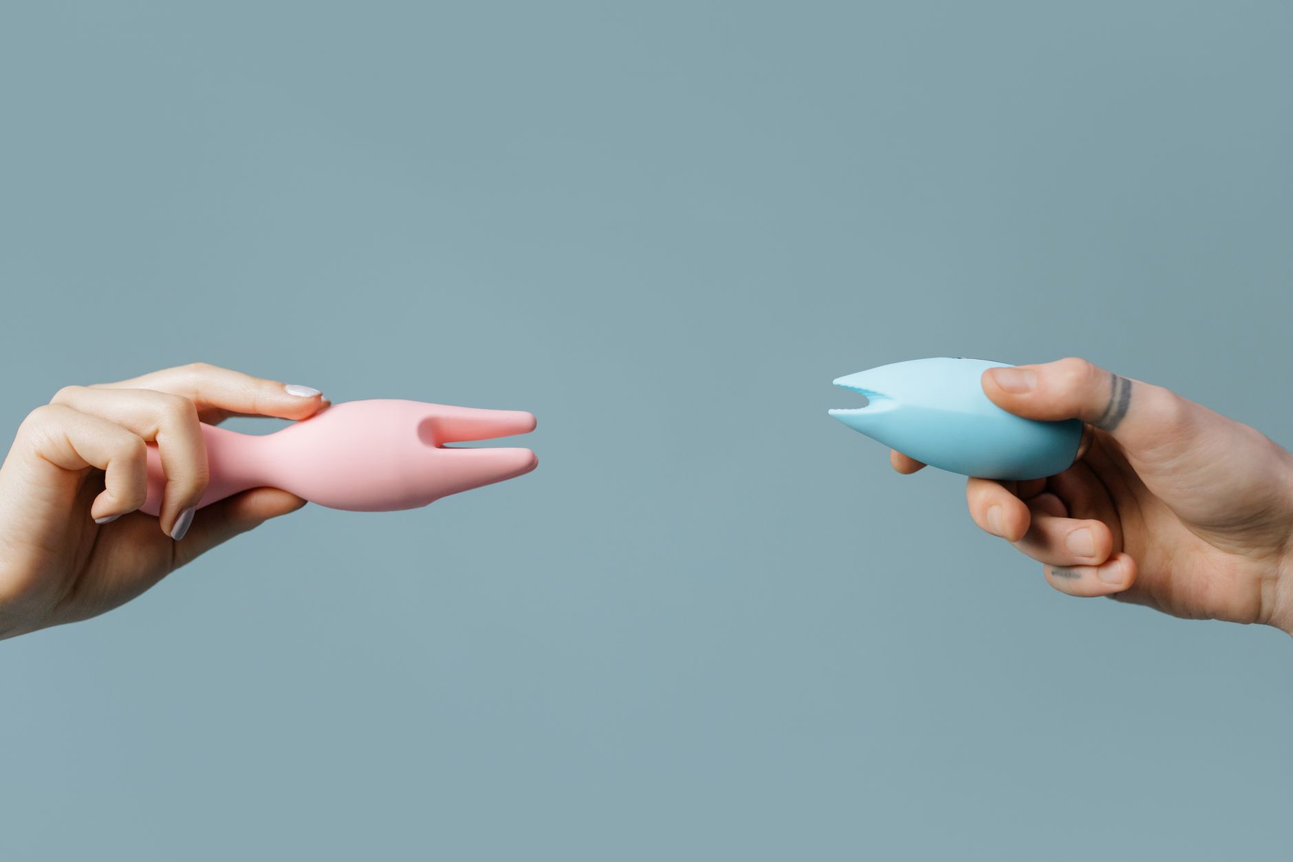 Two hands holding pink and blue silicone vibrators