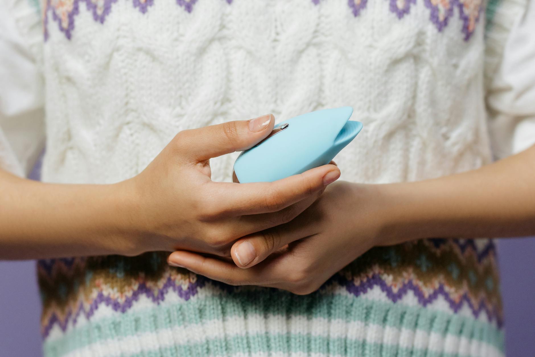 Close-up of hands holding a personal massager against a knitted sweater, representing intimate self-care without time pressure.