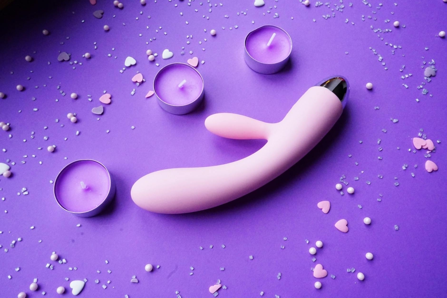 A hand holding a modern orange vibrator against a minimalistic purple backdrop